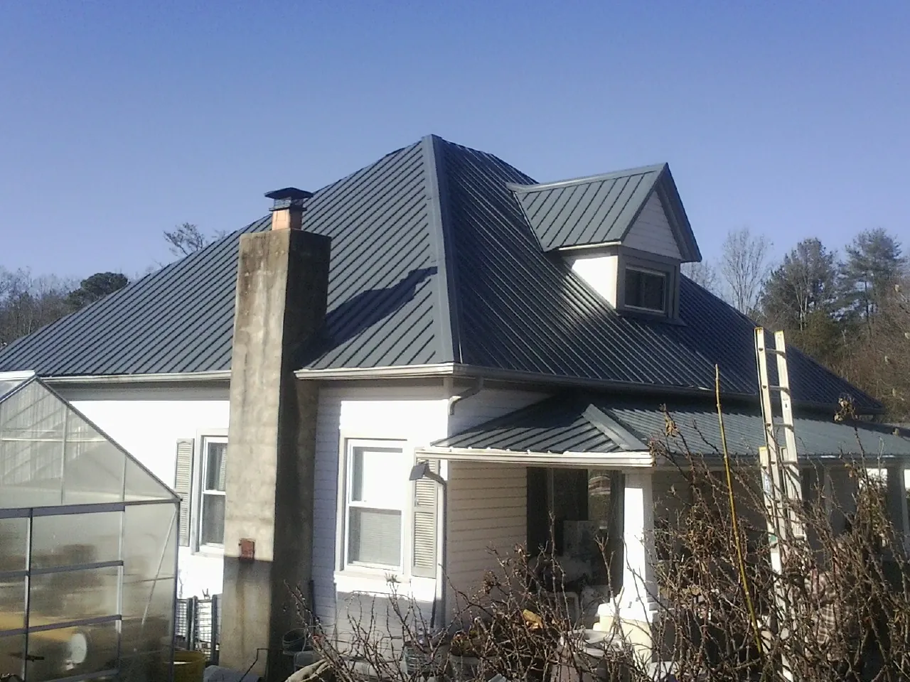 Dark blue standing seam metal roof on a white farmhouse with dormer — Slate & Tile Roof Repair by Roofing Brothers in Owego