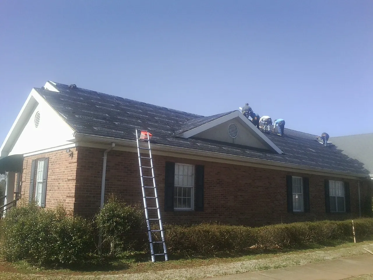 Crew tearing shingles off a brick ranch roof with a ladder set — Emergency Roof Repair work by our crew in Owego