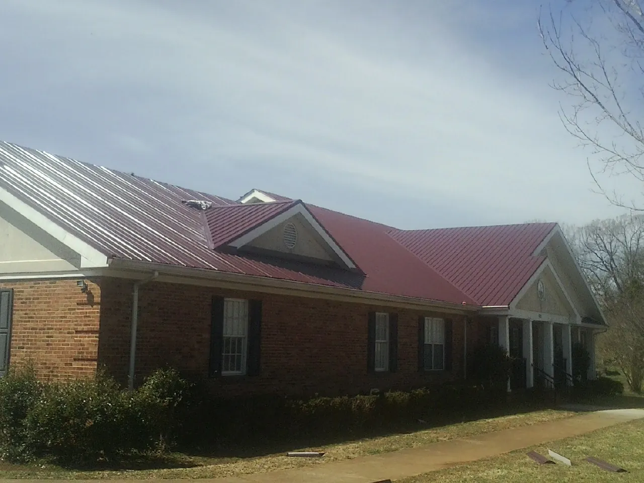 Red metal roof with gabled entries on a long brick building, from a Hail Damage Roof Repair job in Owego