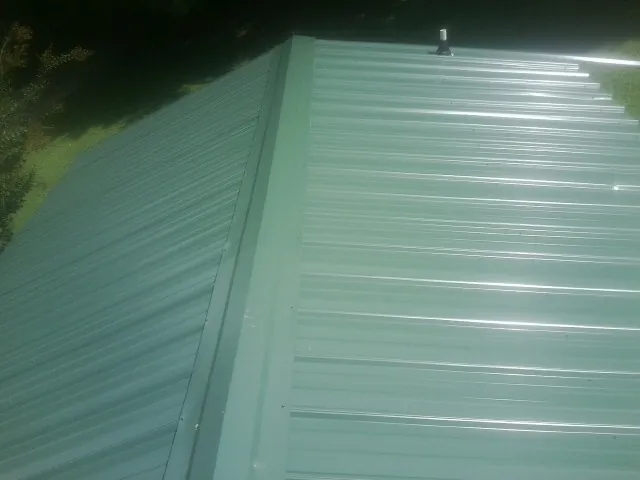 New green metal panels meeting at the ridge of a roof — Flat Roof Repair work by our crew in Owego