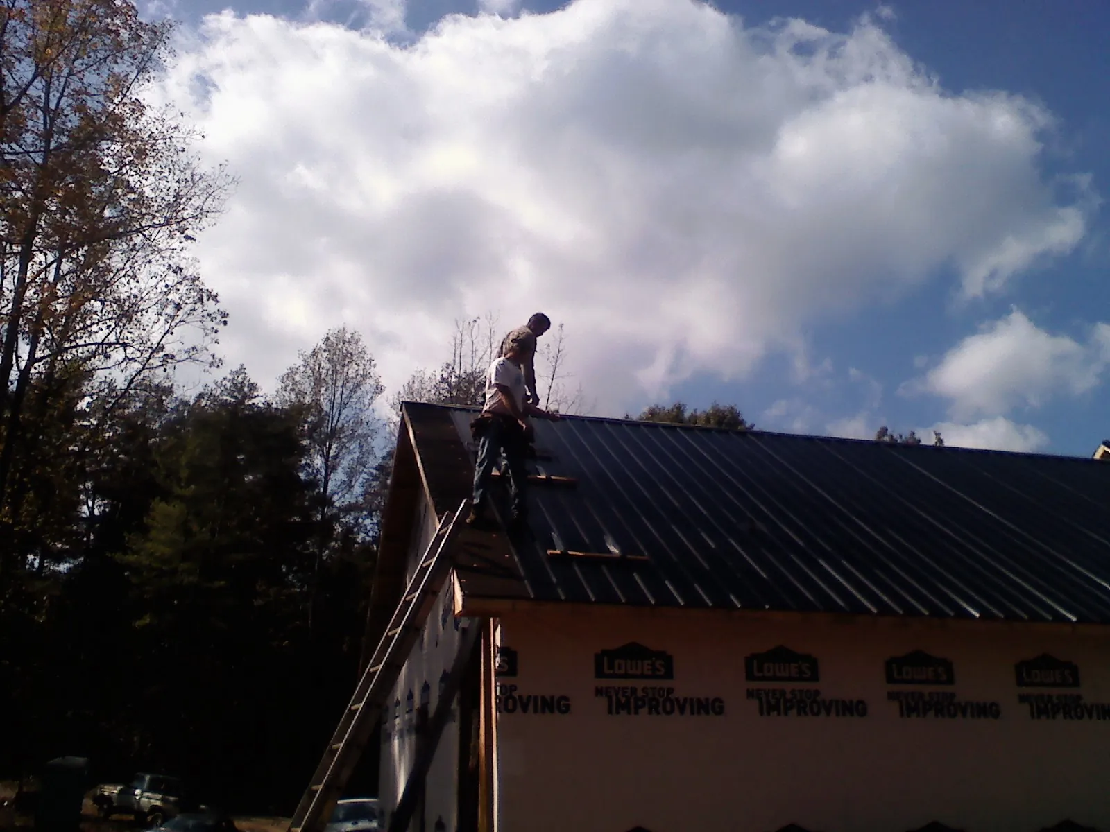 Roofer fastening dark metal panels high against a cloudy sky, from a Roof Inspection job in Owego