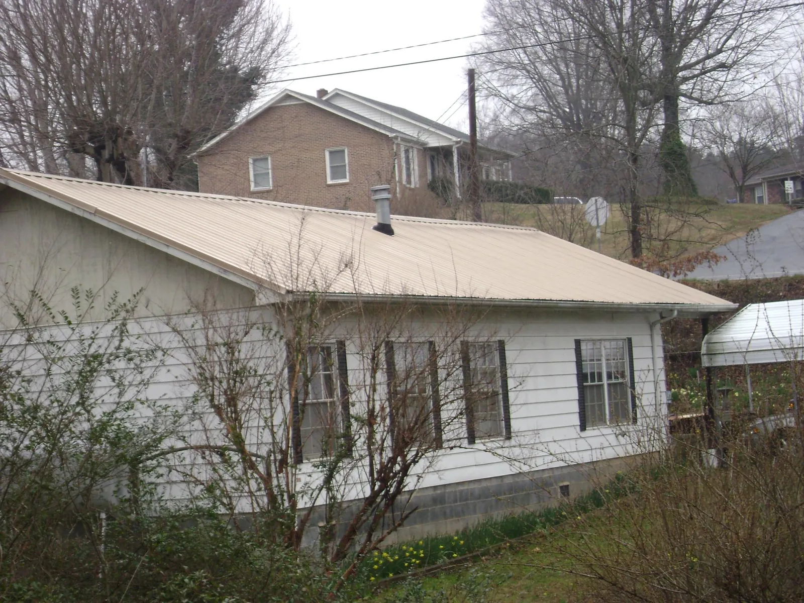 Tan metal roof on a white sided house set into a hillside — Commercial Roofing by Roofing Brothers in Owego
