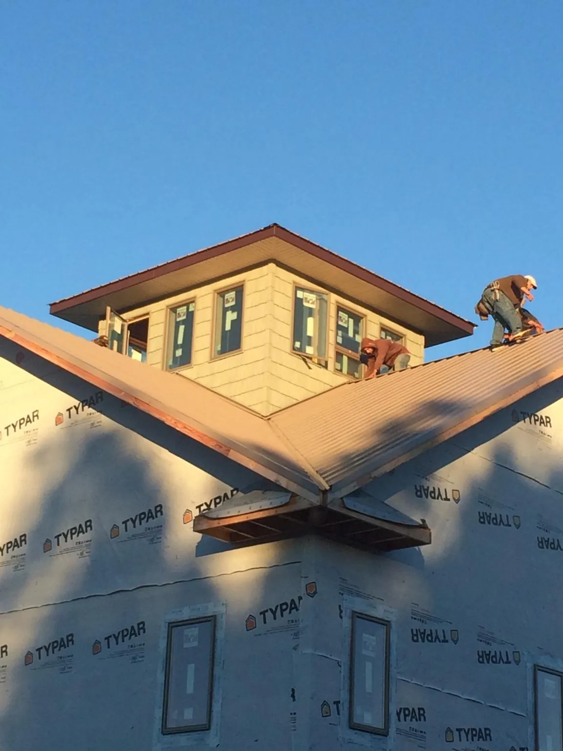 Roofers working around a rooftop cupola on a new metal roof at sunset — Roof Waterproofing in Owego by Roofing Brothers
